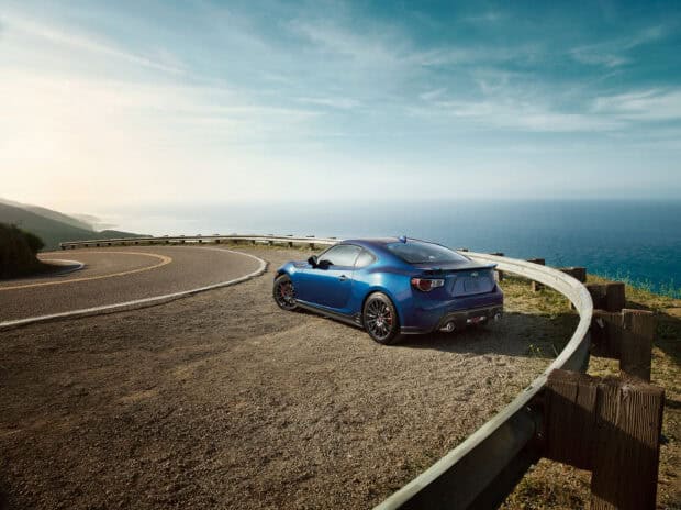 A blue Subaru Brz is parked on a coastal road with the ocean in the background under a clear sky, HD Desktop Wallpaper