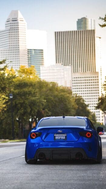 A blue Subaru Brz is parked on an urban road with tall buildings and trees in the background, HD Phone Wallpaper