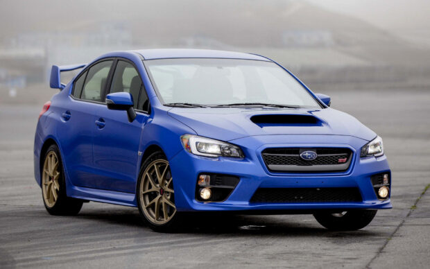 A blue Subaru WRX is parked on a gray asphalt surface with foggy hills in the background, HD Desktop Wallpaper