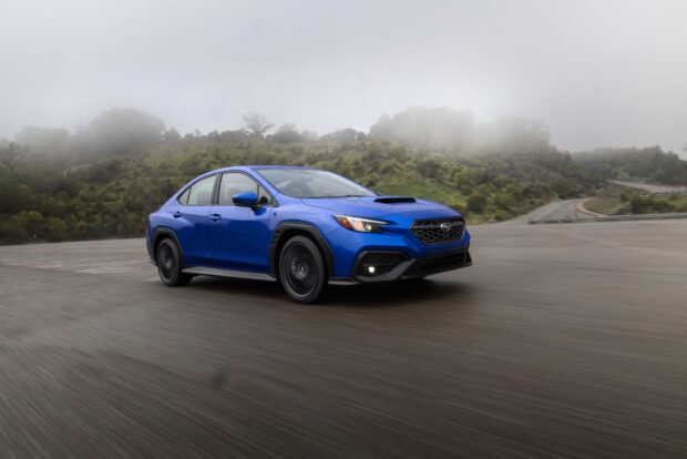 A blue Subaru WRX driving on a wet road with foggy hills in the background, 2K Desktop Wallpaper