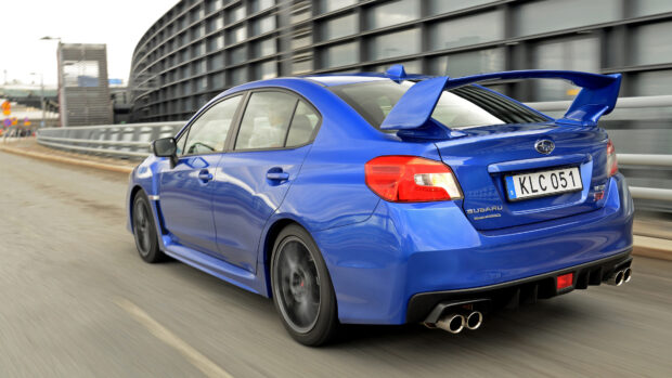 A blue Subaru WRX speeds past urban buildings with motion blur on the wheels, 4K Desktop Wallpaper