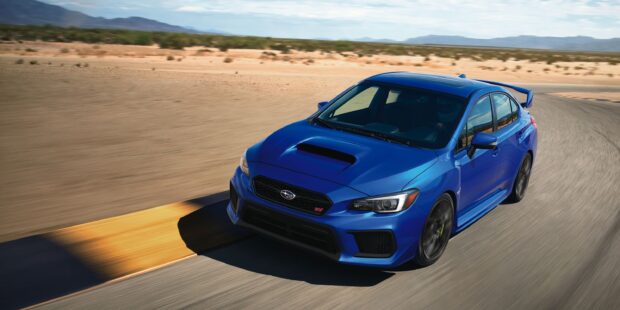 A blue Subaru Wrx speeds along a curved desert road under clear skies, 2K Desktop Wallpaper