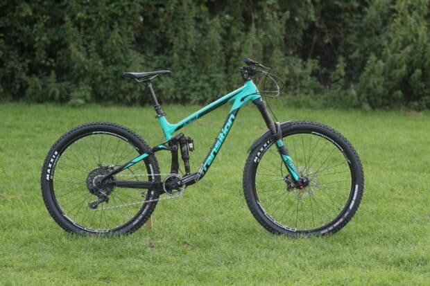 The blue Transition bike stands on a grassy field with dense trees in the background, HD Desktop Wallpaper