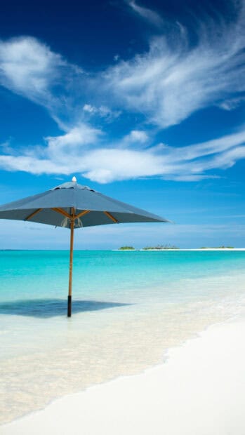 A blue beach umbrella stands in shallow clear water near a white sandy shore with distant islands, 4K Phone Wallpaper