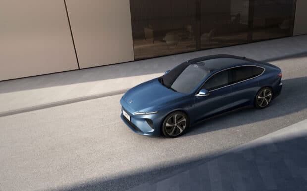 A blue electric sedan is parked alongside modern buildings in this Nio Auto Wallpapers image, 2K Desktop Wallpaper