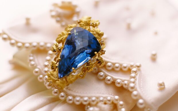 A blue gemstone surrounded by golden leaves lies on a pearl necklace and silky fabric, 2K Desktop Wallpaper