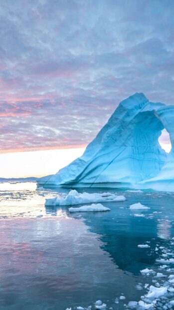 A large blue glacier arch is reflected in calm icy water during sunset, 4K Phone Wallpaper