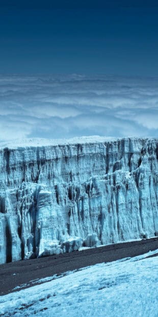 A blue glacier cliff towering above the snowy ground with clouds in the background, 2K Mobile Wallpaper