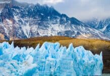 The glacier shows bright blue ice details beneath rugged brown mountains, 4K Desktop Wallpaper