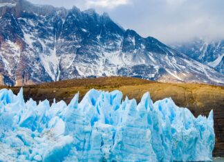 The glacier shows bright blue ice details beneath rugged brown mountains, 4K Desktop Wallpaper