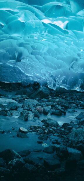 A stunning glacier ice formation glows blue above a rocky and icy ground, 2K Mobile Wallpaper