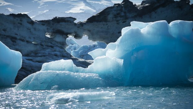 A stunning view of blue glacier ice formations next to water and rocks, 4K Desktop Wallpaper