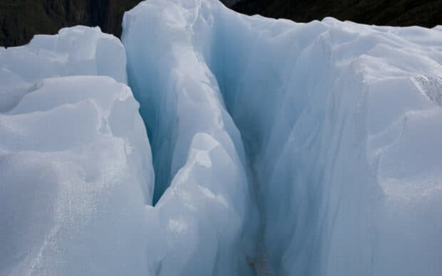 The glacier showcases bright blue ice formations with deep crevices under cloudy skies, 2K Desktop Wallpaper