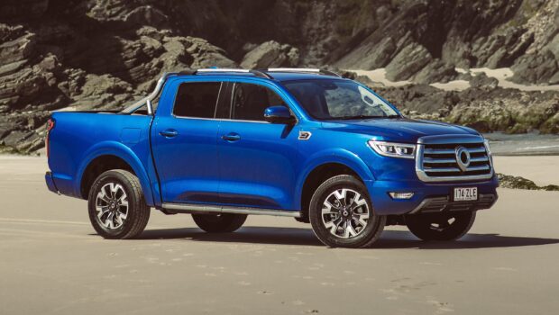 A blue pickup truck from Great Wall Motors is parked on a sandy beach with rocky cliffs behind, 2K Desktop Wallpaper
