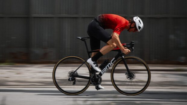 A cyclist wearing a red jersey rides a Bmc bike at high speed on the street, 2K Desktop Wallpaper