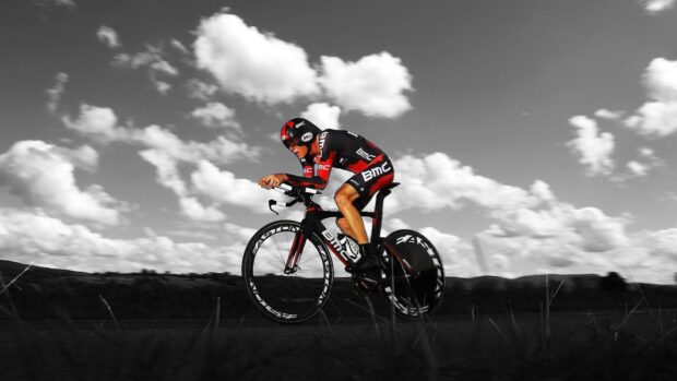 A cyclist wearing Bmc Bikes gear races on a road under a cloudy sky, HD Desktop Wallpaper
