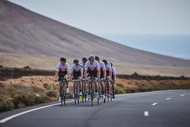 A group of cyclists riding Bmc Bikes together on a paved road with mountainous landscape, HD Desktop Wallpaper