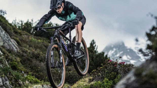 A cyclist riding a Bmc bike jumps over rocky terrain in the mountains, HD Desktop Wallpaper