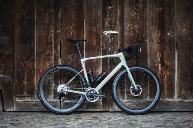 A Bmc bike is parked in front of a rustic wooden wall with cobblestone ground, HD Desktop Wallpaper