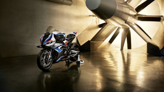 A BMW M 1000 Rr stands in an industrial room with a large metal turbine behind it, 4K Desktop Wallpaper