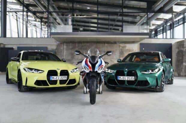 A Bmw M 1000 Rr motorcycle stands between two BMW sports cars in an industrial setting, HD Desktop Wallpaper