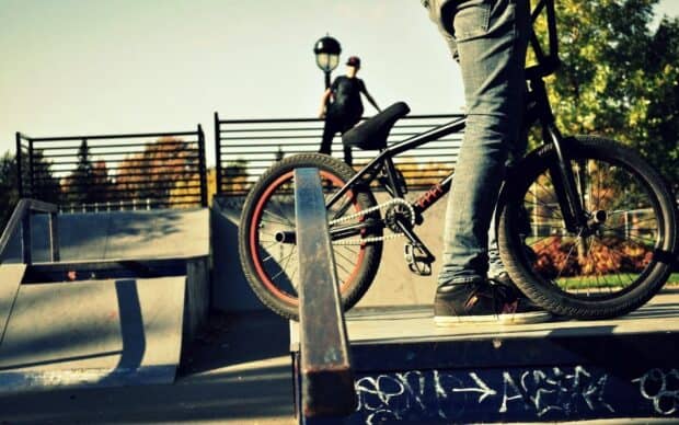 A BMX sports rider stands with his bike near a skatepark rail under autumn trees, HD Desktop Wallpaper