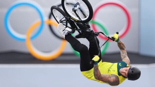A BMX rider wearing a yellow jersey is mid air performing a trick with the Olympic rings in the background, 2K Desktop Wallpaper