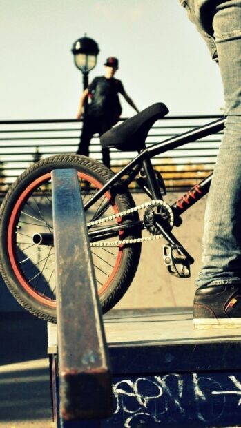 A BMX sports bike is positioned near a ramp with a person standing behind wearing casual clothes, HD Mobile Wallpaper
