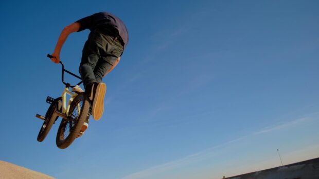 A BMX rider performs a jump against a clear blue sky during a sunny day, HD Desktop Wallpaper