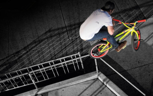 A BMX sports rider is jumping over a handrail performing a trick in an urban setting, HD Desktop Wallpaper