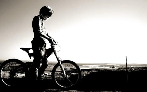 A BMX sports rider wearing a helmet stands with a bike overlooking the cityscape, 2K Desktop Wallpaper