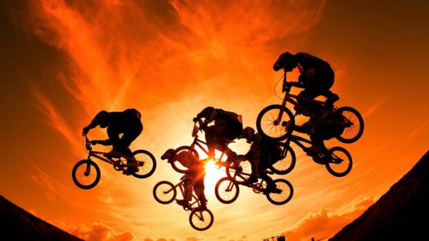 A group of Bmx sports riders are captured mid air against a vibrant orange sunset sky, HD Desktop Wallpaper