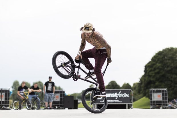 A tattooed man performs a BMX sports trick at a skate park while others watch, 2K Desktop Wallpaper