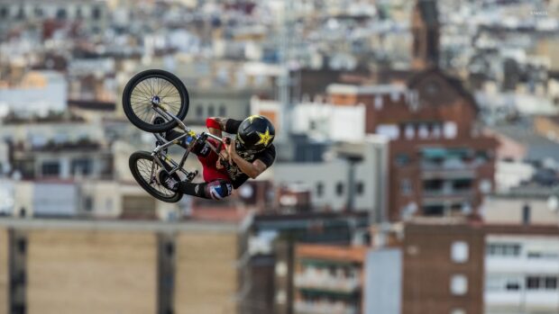 A BMX sports rider is performing a trick high above city buildings, HD Desktop Wallpaper