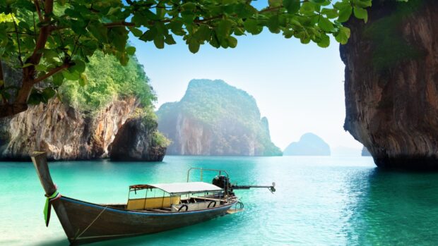 A traditional boat floats on turquoise water near limestone cliffs in Phuket, HD Desktop Wallpaper