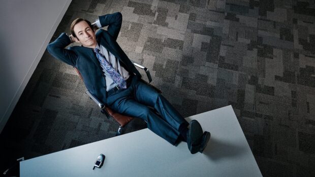 Bob Odenkirk is seated casually with his hands behind his head in a modern office setting, HD Desktop Wallpaper