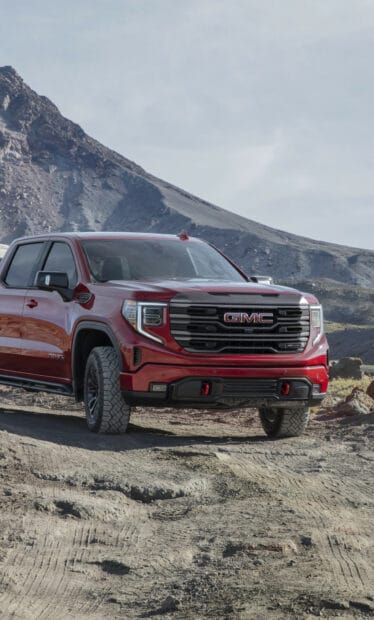 A bold red GMC Sierra truck parked on a rocky dirt path with mountains in the background, HD Mobile Wallpaper