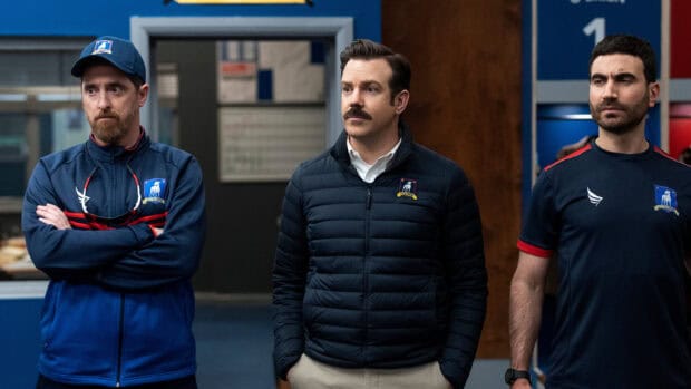 Brett Goldstein and two men stand in a sports facility wearing team jackets, 2K Desktop Wallpaper