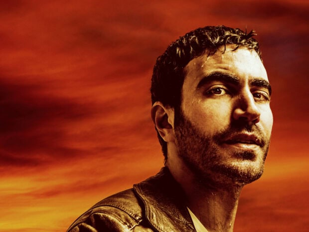 Brett Goldstein is seen against a fiery orange sky in a close up portrait, HD Desktop Wallpaper