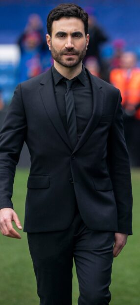 Brett Goldstein is walking confidently dressed in a black suit and tie, HD Mobile Wallpaper