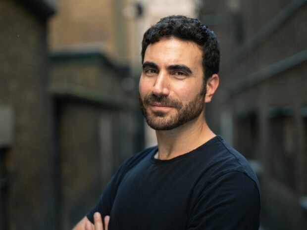 Brett Goldstein is standing with folded arms in an urban setting, HD Desktop Wallpaper
