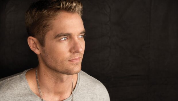 Brett Young wallpapers show a man with blue eyes wearing a gray shirt against a dark background, 2K Desktop Wallpaper