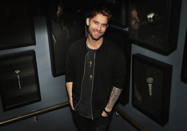 Brett Young smiles with his tattooed arm visible as he stands near black framed microphones, 2K Desktop Wallpaper