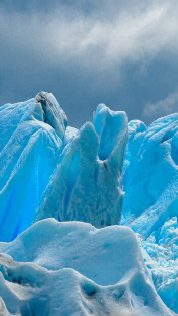 Bright blue glacier ice formations under a cloudy sky, 2K Phone Wallpaper