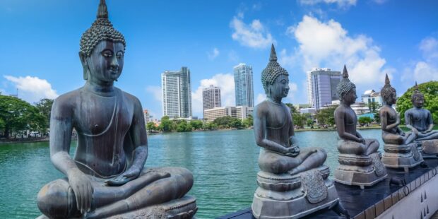 A row of Buddha statues sits peacefully beside a lake with Colombo city skyscrapers in the background, HD Desktop Wallpaper