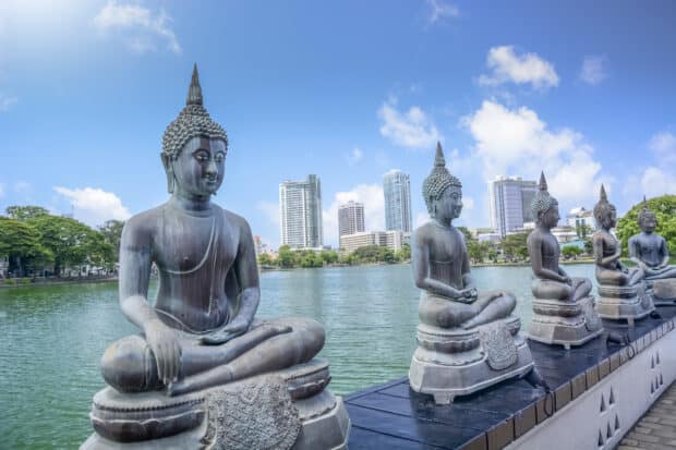 Buddha statues are seated by a lake with city buildings in the background in Colombo Sri Lanka, HD Desktop Wallpaper