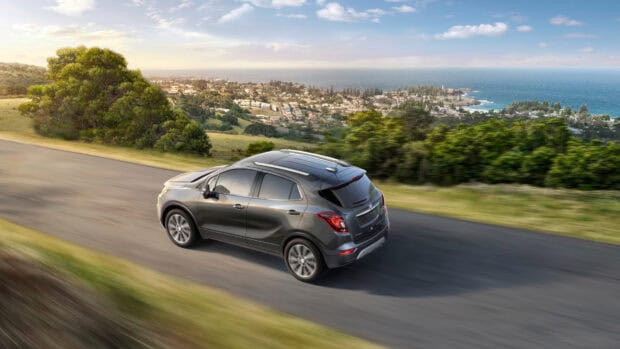 A gray Buick Encore driving along a coastal road with greenery and ocean in the background, 4K Desktop Wallpaper