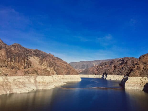 A calm view of Lake Mead with rocky cliffs under a clear blue sky, HD Desktop Wallpaper