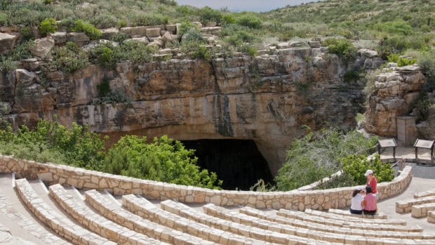 Visitors explore the Carlsbad Caverns National Park entrance with rocky surroundings and greenery, HD Desktop Wallpaper
