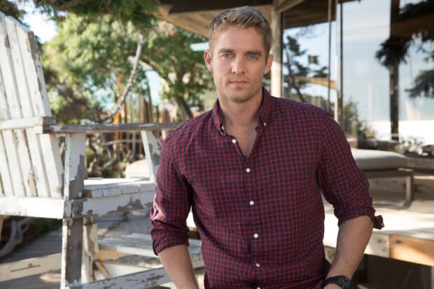 A casual portrait of Brett Young standing outside near wooden chairs with trees in the background, HD Desktop Wallpaper